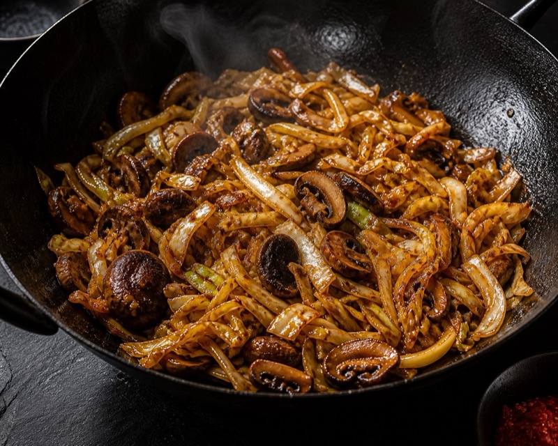 Oosterse spitskool met champignons in ketjap en sambal in een zwarte wok
