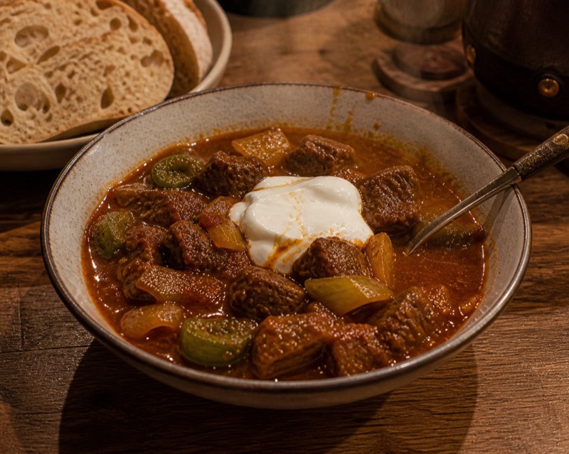 Hongaarse goulash met groene paprika en zure room, brood op de achtergrond
