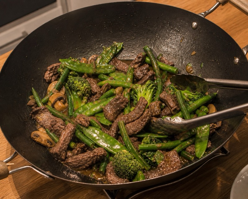 Snelle wokmaaltijd met biefreepjes, sperziebonen, peultjes en broccoli in een wok